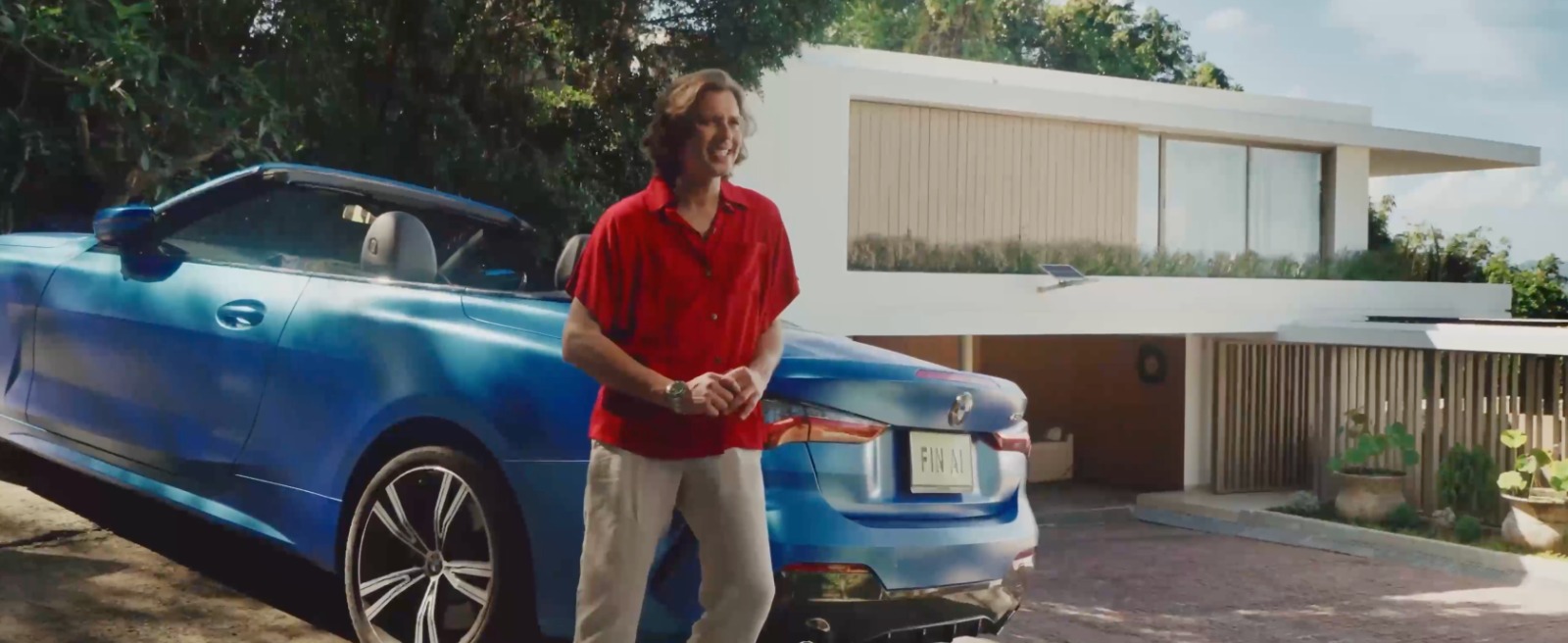 A founder standing beside a blue car outside a modern home